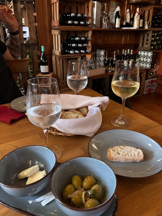 Weißwein, Brot und Oliven vor dem Weinregal